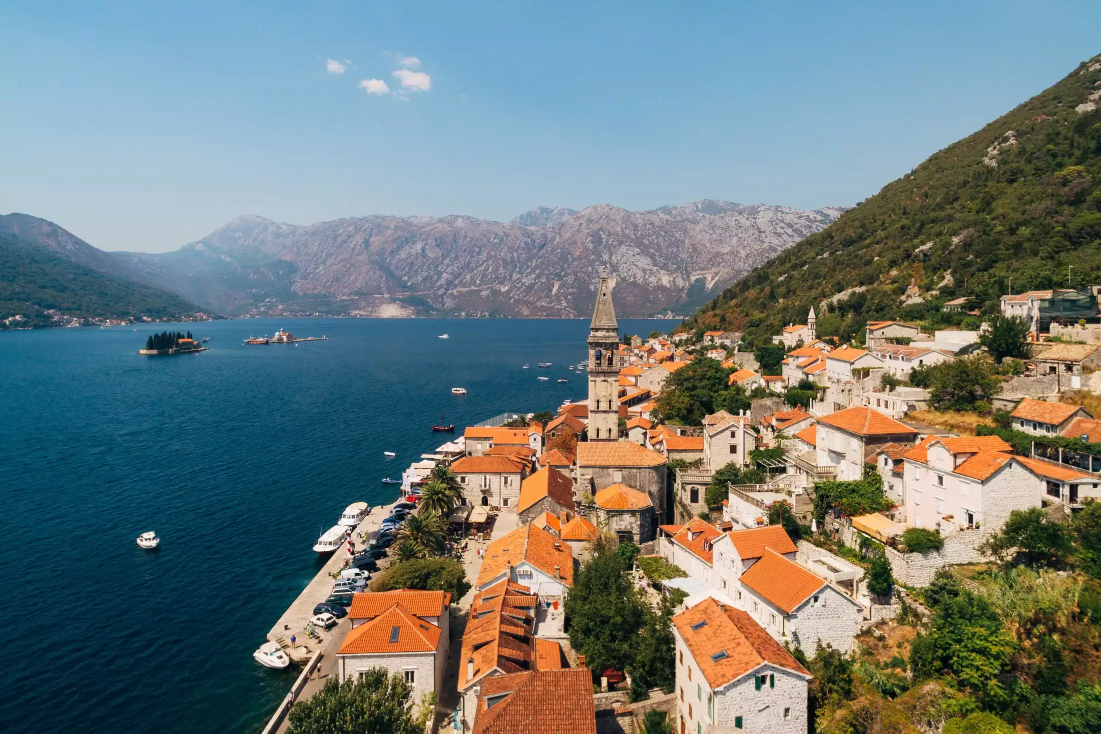 A view of Perast Montenegro from above showing red-roofed stone houses of the old town and the Bay of Kotor in the background.